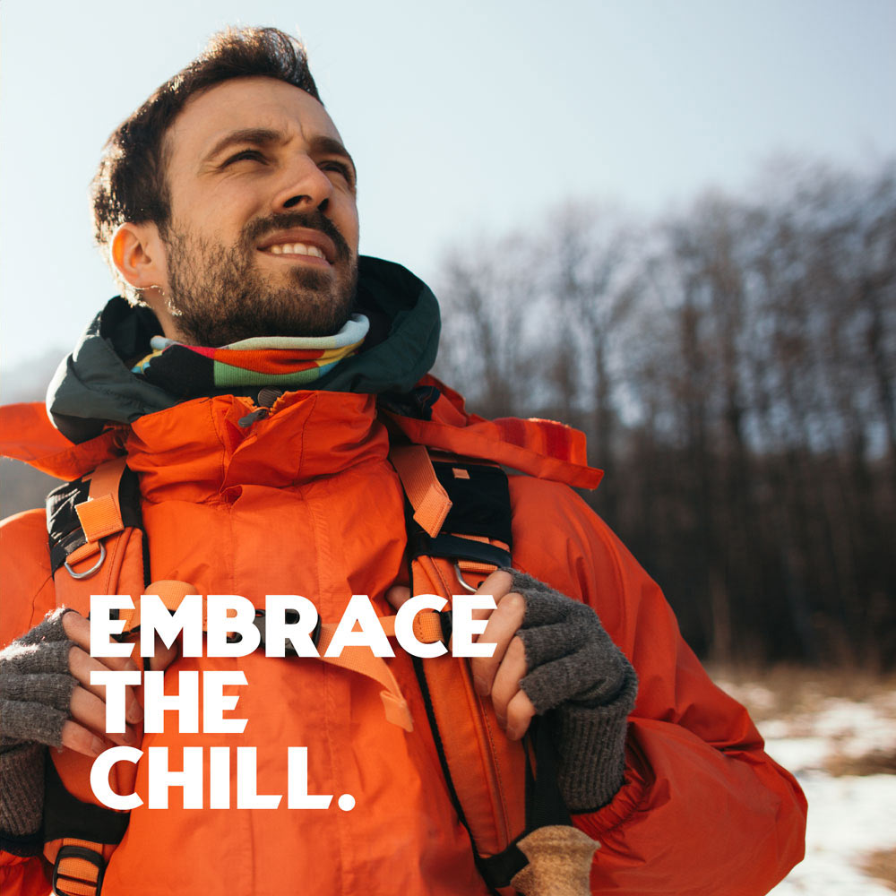 Photo of a smiling man wearing warm ski clothing, with snow on the ground and trees in the background. There is a headline on top saying "Embrace the chill".